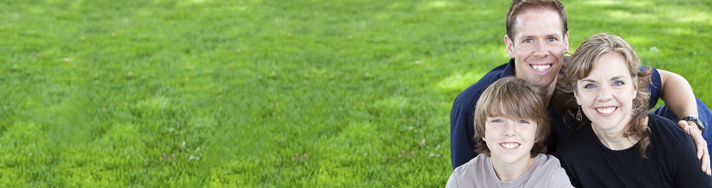 Family of three smiling while sitting in the grass