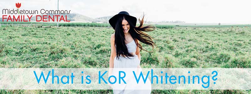 Woman in black hat and white dress smiling while walking through a field