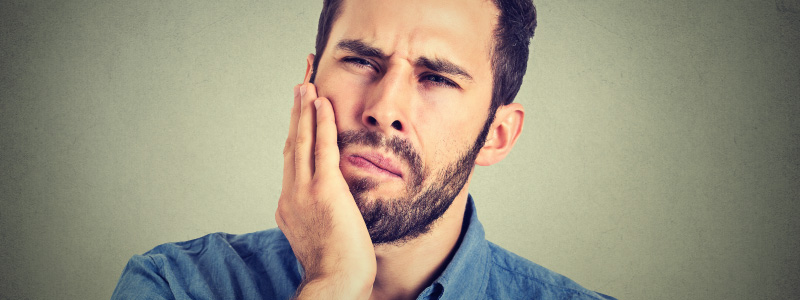 brunette man with facial hair holding mouth in pain