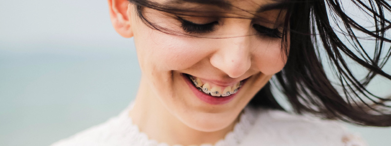Dark-haired woman with braces looks down and smiles as her hair blows in the wind