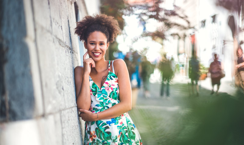 Curly-haired woman wearing a floral summer dress after root canal therapy smiles pain-free