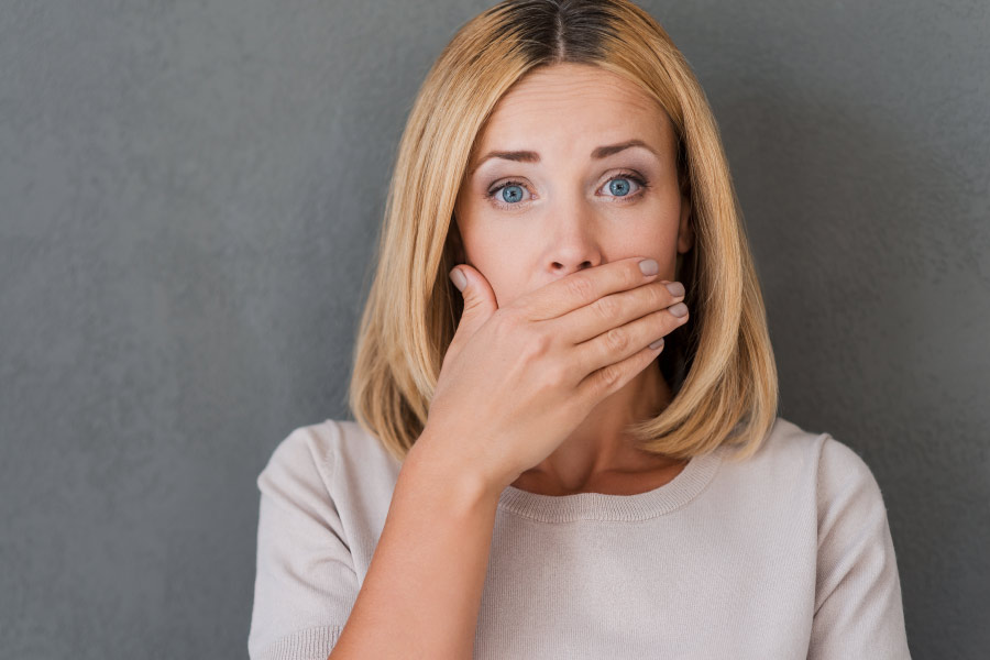 Blonde woman covering her mouth with her hand because she's worried about bad breath.