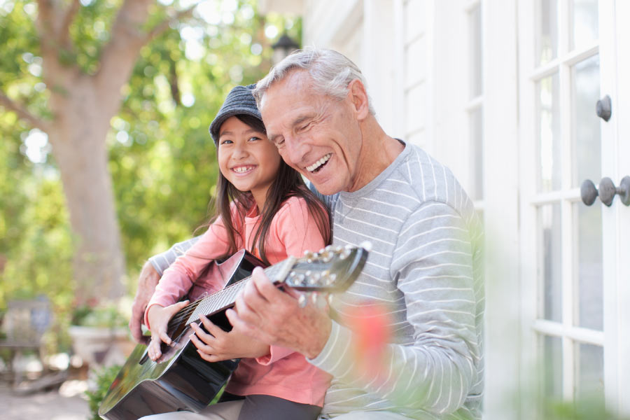 Smiling man playing the guitar with his granddaughter.