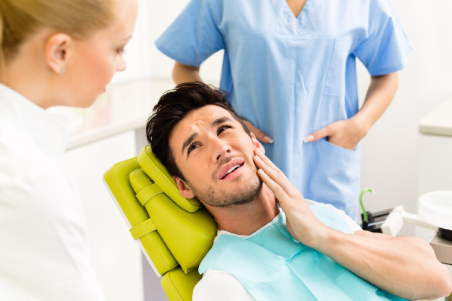 Man in the dental chair with his hand on his cheek due to jaw pain.