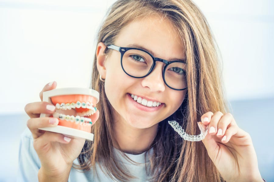 Teen holding a model of a  mouth with braces in one hand and a clear aligner in the other.