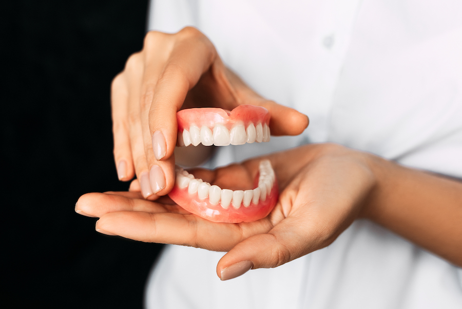 Photograph of dental provider holding dentures. Accompanies article about eating with dentures.